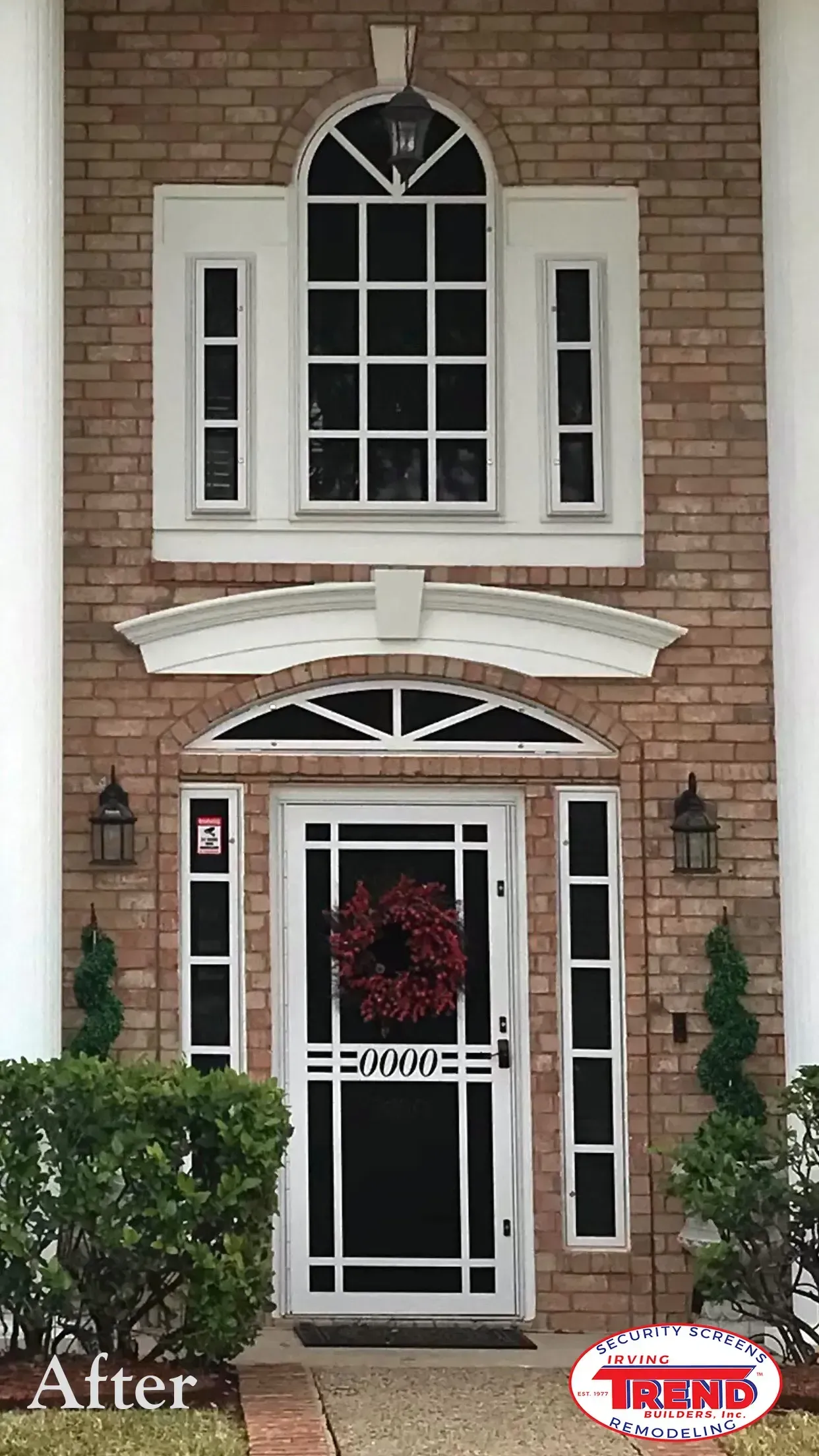 The front door of a brick house with a screen door and a wreath on it.