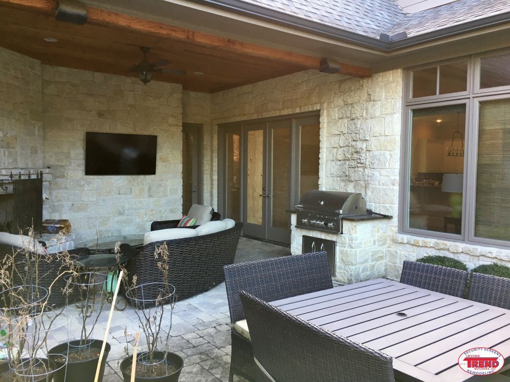 A patio with a table , chairs , a television and a grill.