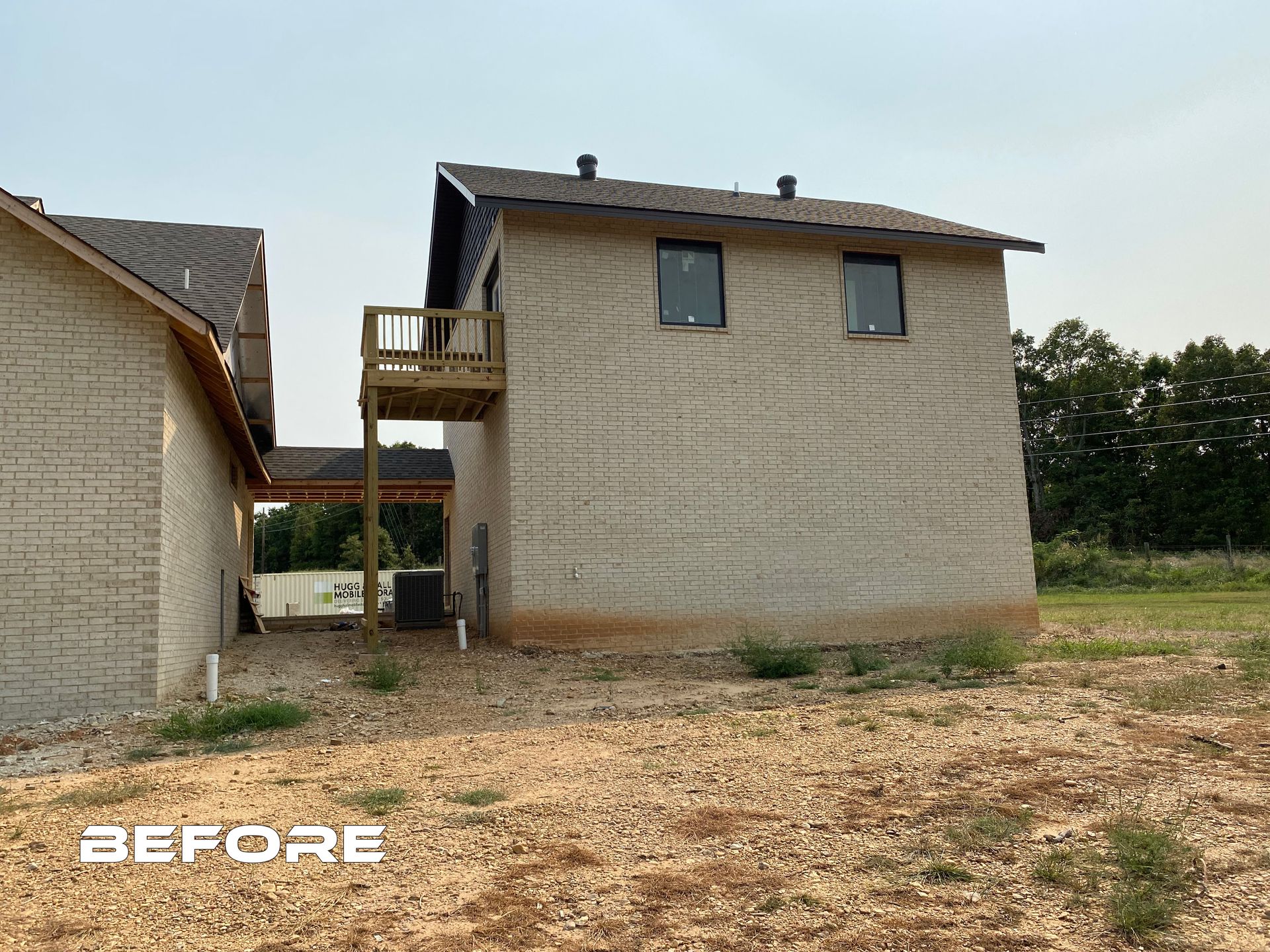 A brick house with a balcony is sitting on top of a dirt field.