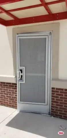 A white door with a screen on it is on a brick building.