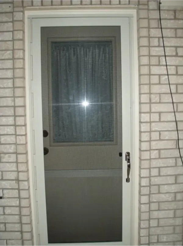 A door with a screen on it is against a white brick wall
