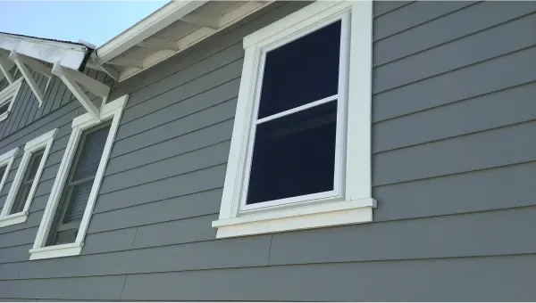 A gray house with white trim and two windows on the side.