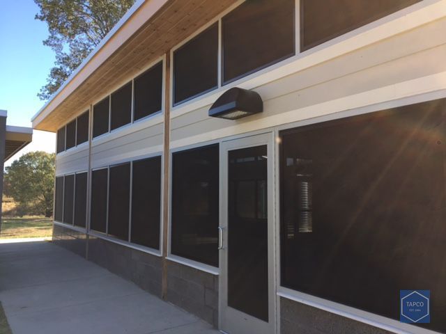 Exterior of a screened building with beige siding, a gray door, and a concrete patio.