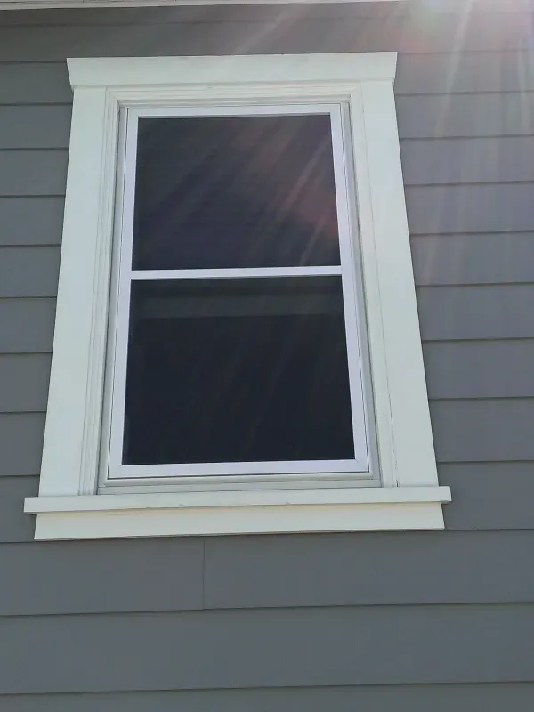 A window on the side of a house with the sun shining through it