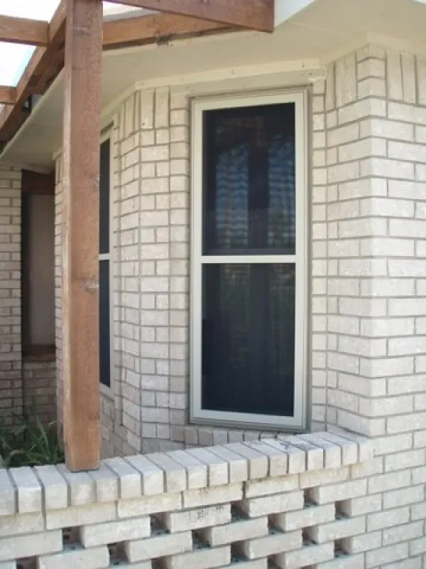 A white brick building with a window and a wooden pergola