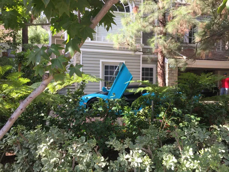 A blue car is parked in front of a house with its hood open