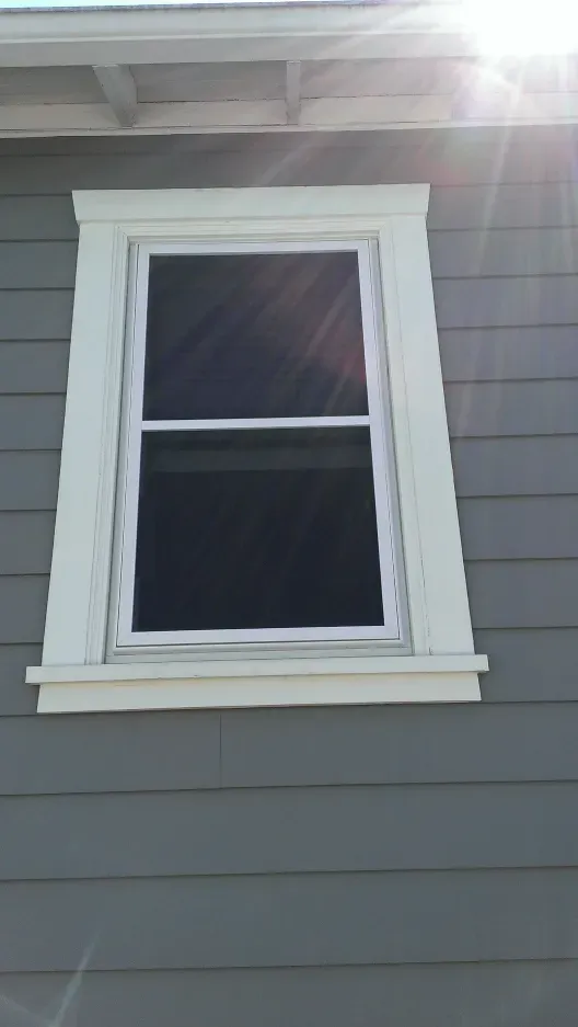 A window on the side of a house with the sun shining through it.