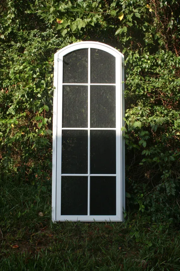 A white window with black screens is sitting in the grass