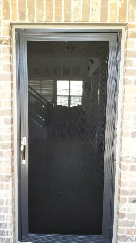 A black screen door is sitting on top of a brick wall.