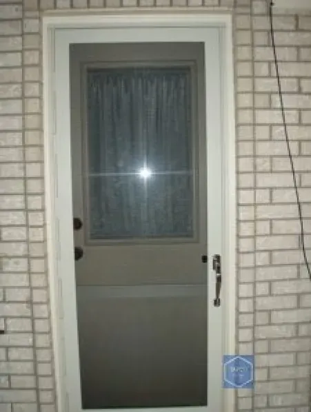 A screen door is on a white brick wall.