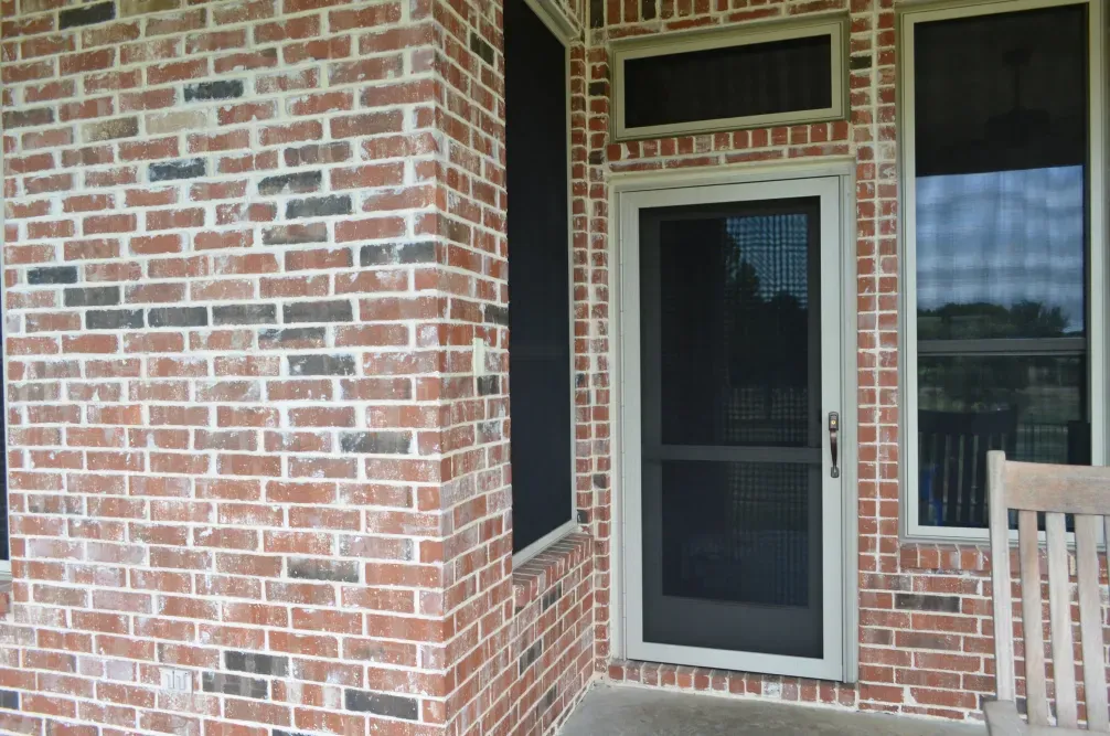 A brick building with a screen door and a chair