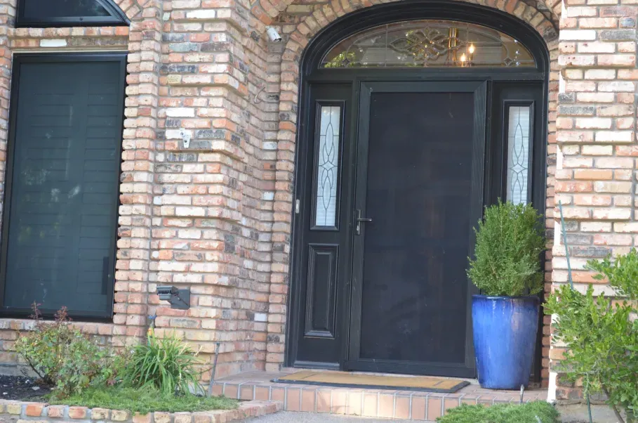 A brick house with a black door and a blue potted plant in front of it.