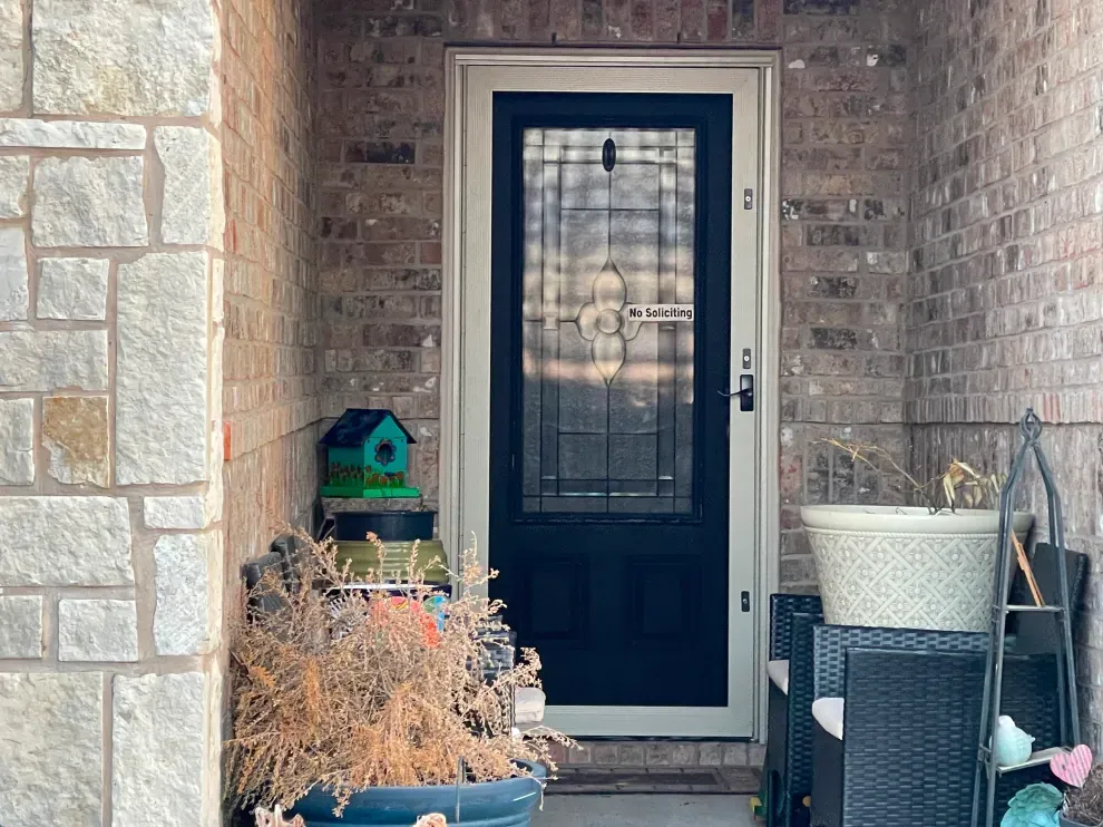 A black door is sitting on a porch next to a brick wall.