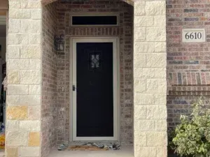 The front door of a brick house with a screen door.