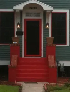 A green house with red steps and a red door