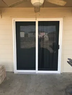 A sliding glass door with a screen on it is on a patio with a ceiling fan.