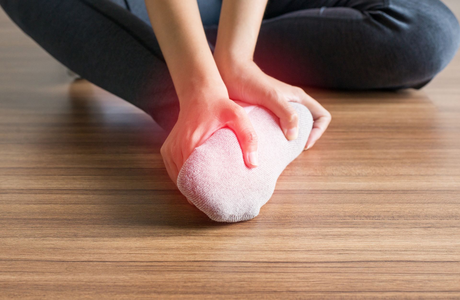 Person sitting cross-legged holding heel with pain highlight