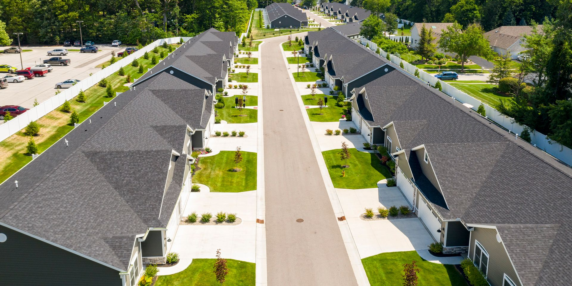 Aerial view of a residential street with rows of gray-roofed townhouses and a central sidewalk.