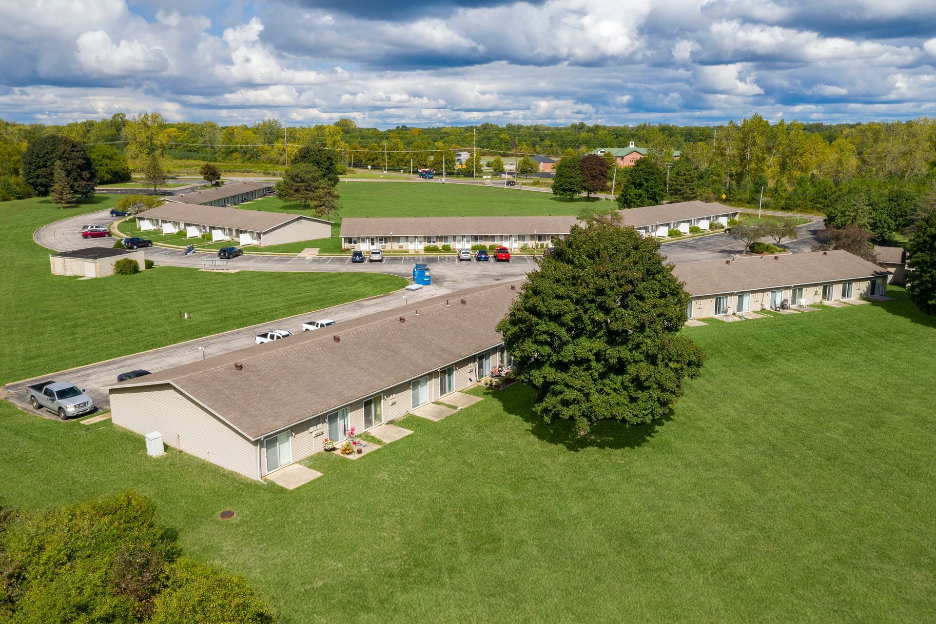 Aerial view of low buildings and a large green lawn in a rural campus under a cloudy sky.