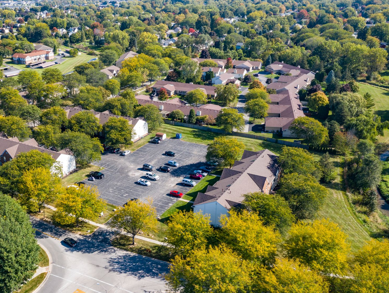 Aerial view of a large building complex with parking lot, surrounded by trees and greenery
