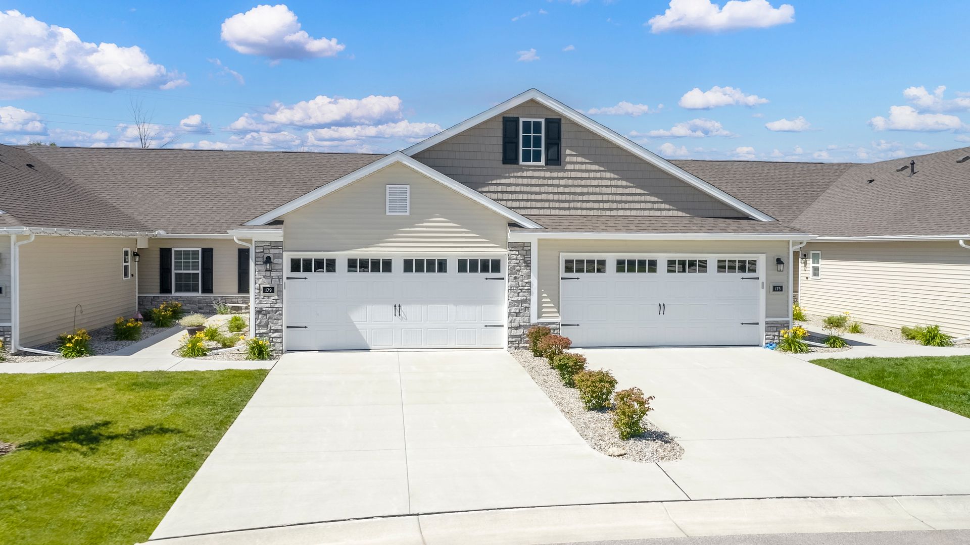 Row of beige townhouses with white garages and driveways under a blue sky