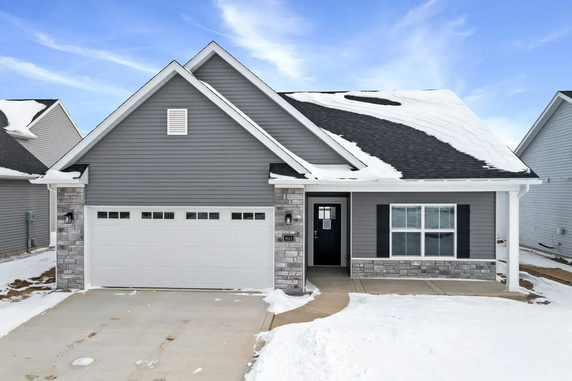 Snowy suburban house with gray siding, white trim, and a two-car garage