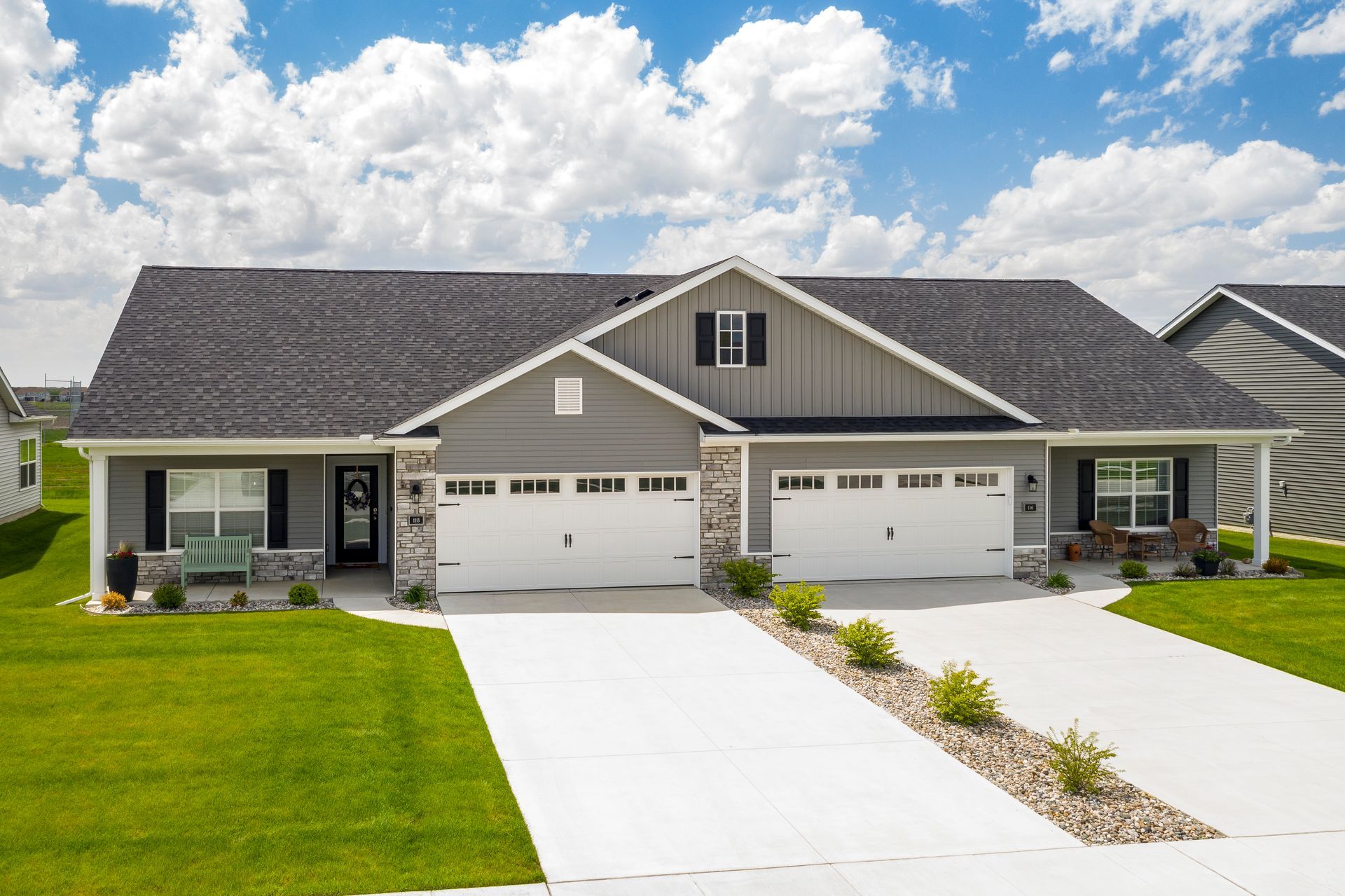Suburban duplex with two white driveways, gray siding, and green lawns under a cloudy sky