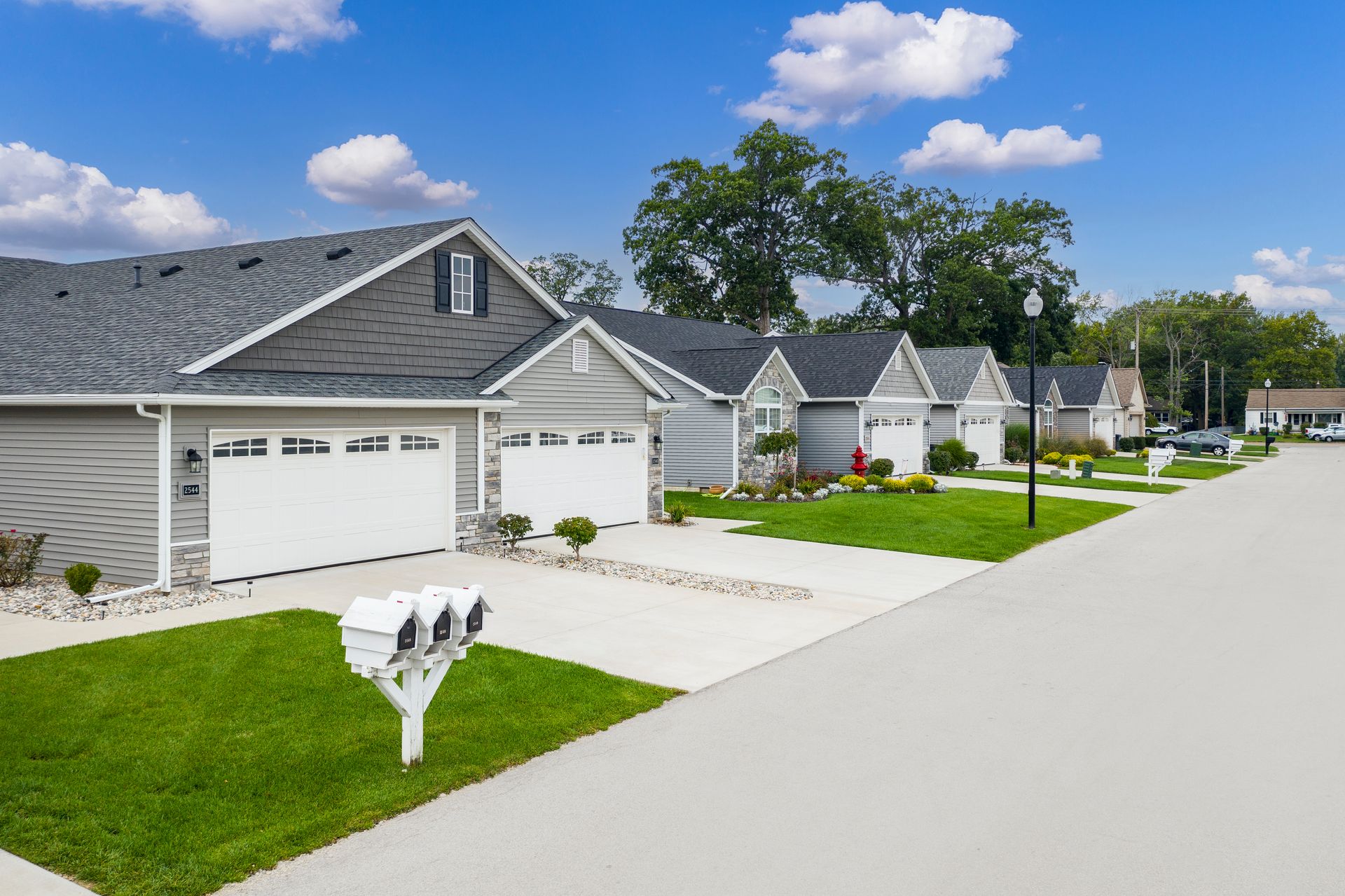 Suburban street with row of gray houses, green lawns, and bright blue sky with clouds