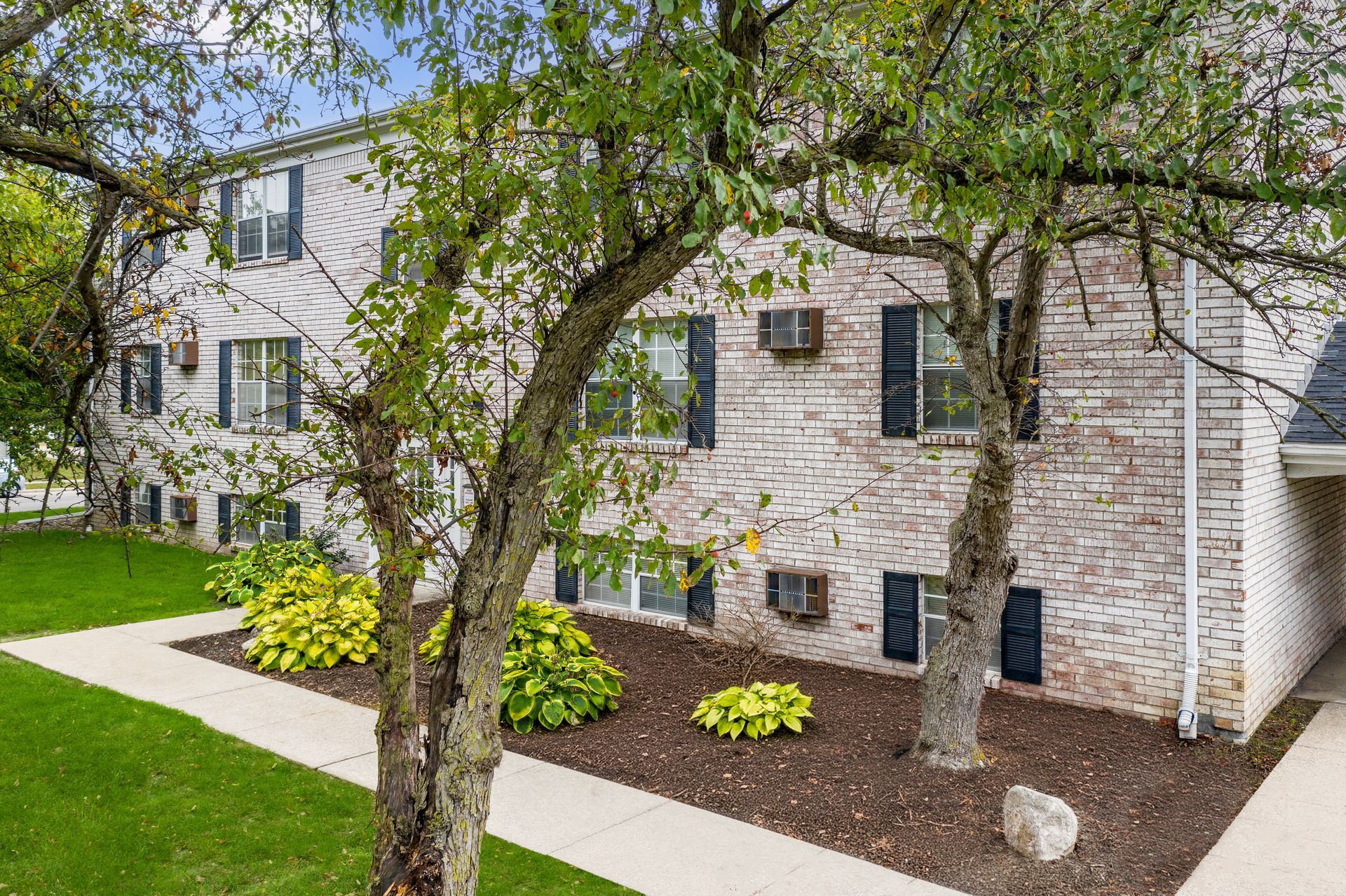 Apartment building with brick exterior, trees, and a sidewalk in front