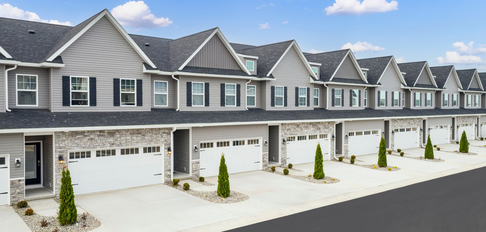 Row of modern gray townhouses with attached garages and small landscaped yards under a blue sky