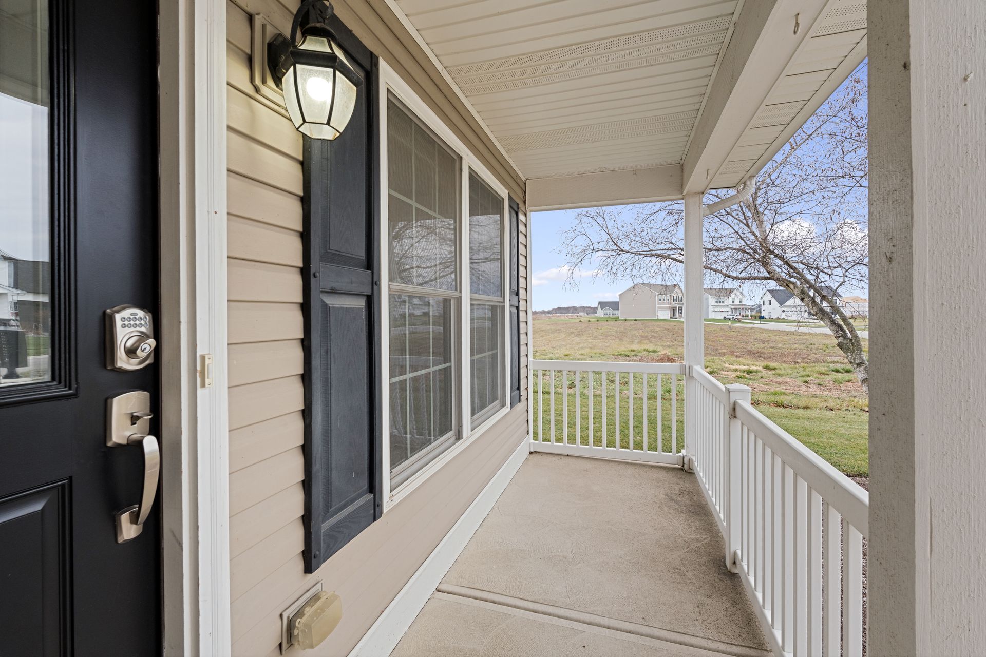 Front porch with beige siding, black shutters, white railing, and a view of open fields beyond.