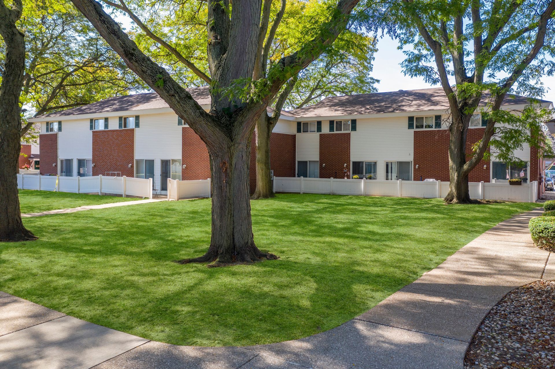Apartment courtyard with trees, green lawn, and a sidewalk in front of brick buildings