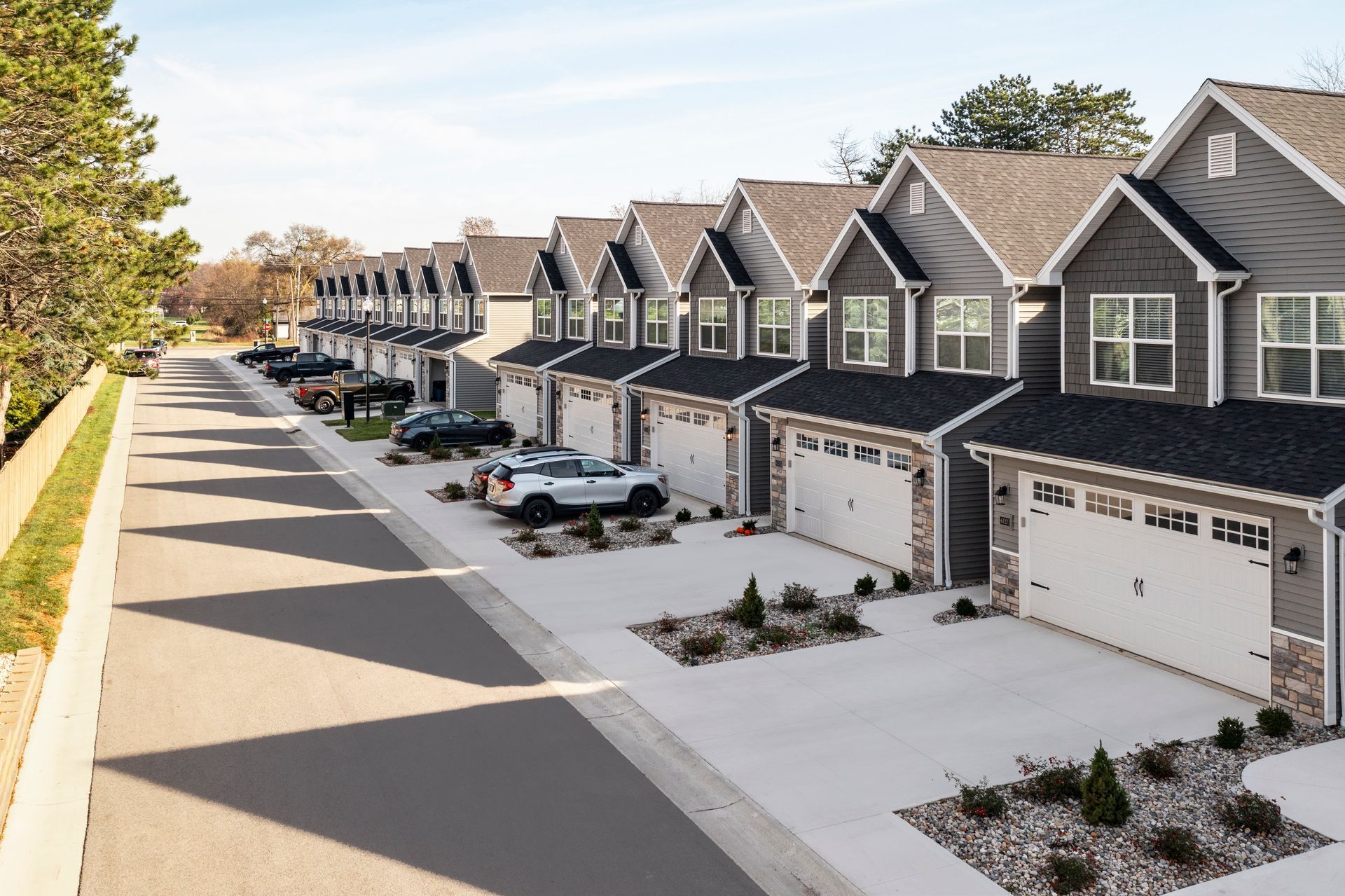 Row of modern gray townhouses with garages along a quiet residential street at sunset