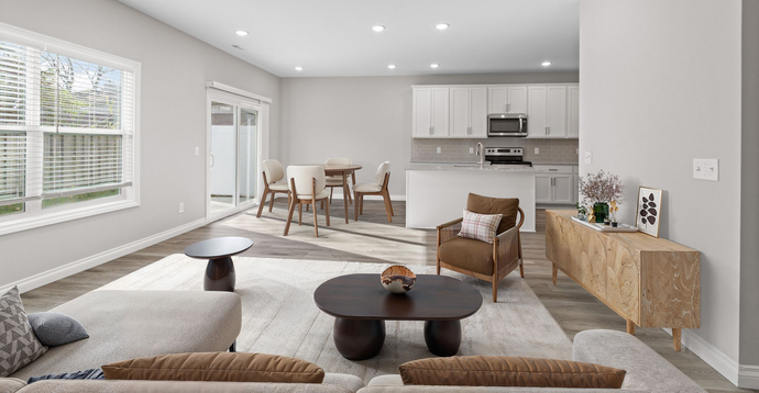 Bright modern living room with gray sofa, coffee tables, dining area, and kitchen in the background
