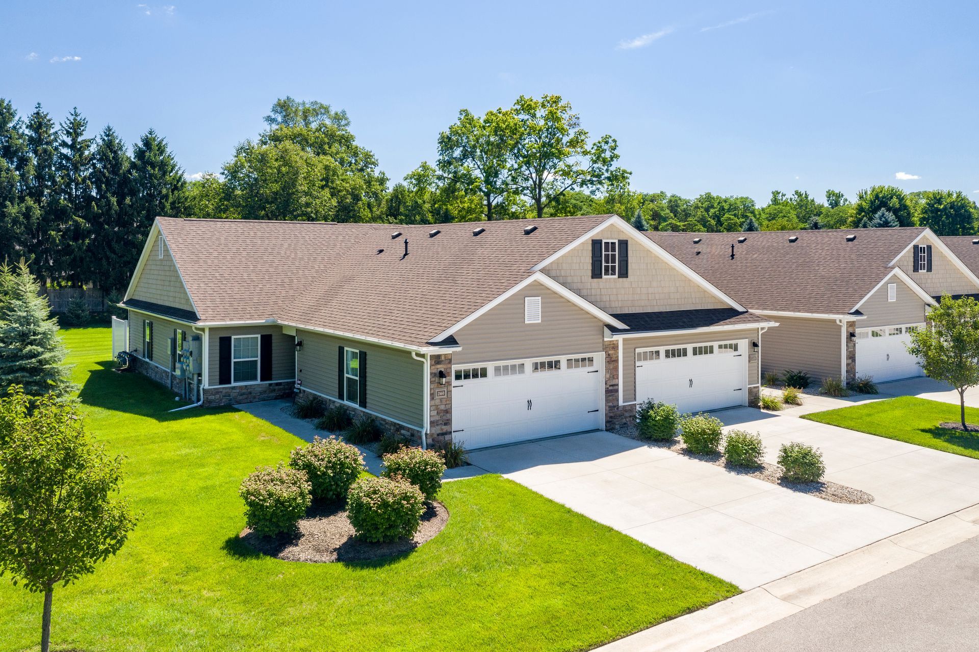 Single-story suburban house with beige siding, white garage, and a green lawn on a sunny day
