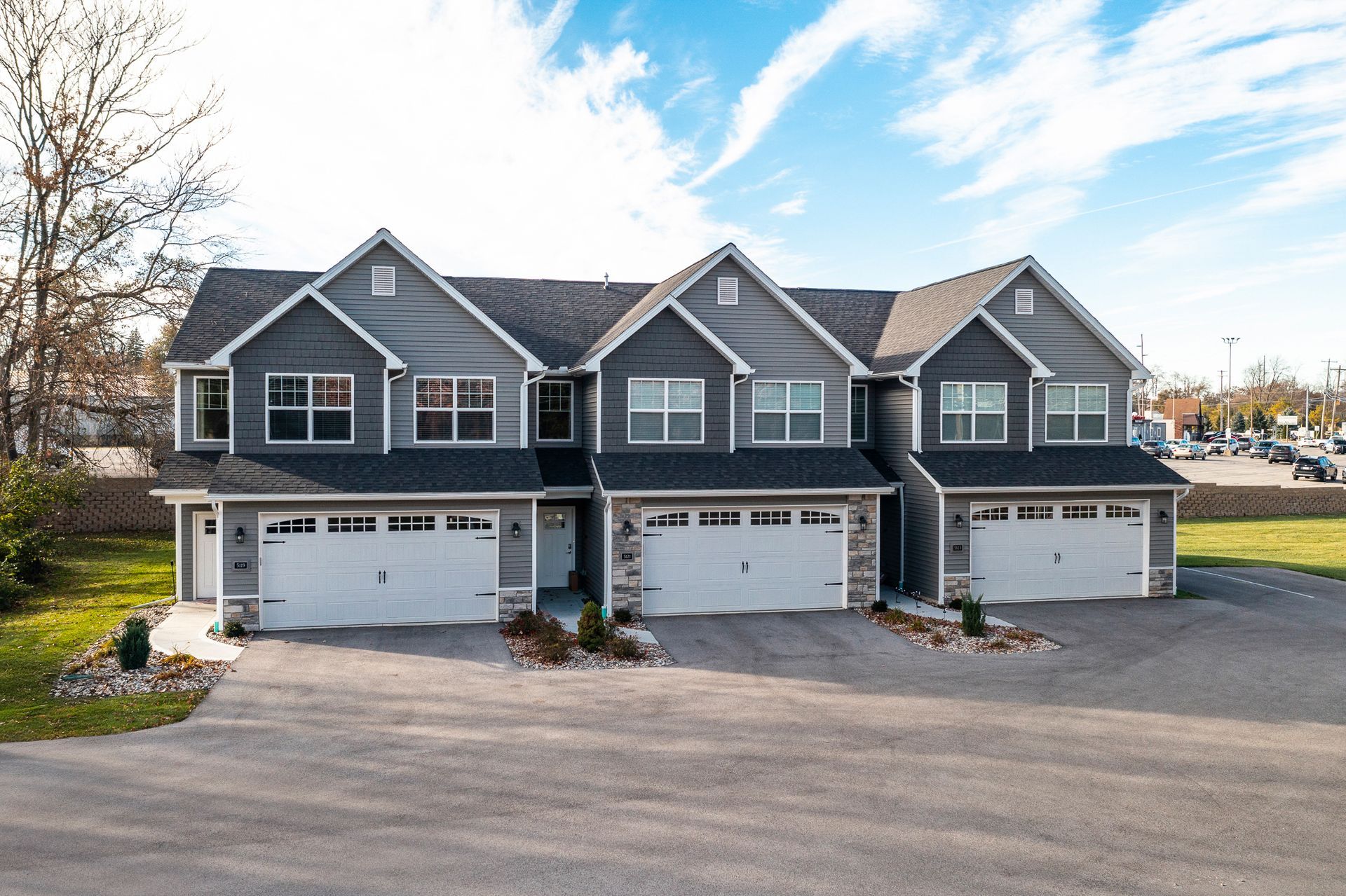 Three gray townhouse units with attached garages and dormer windows along a paved drive.
