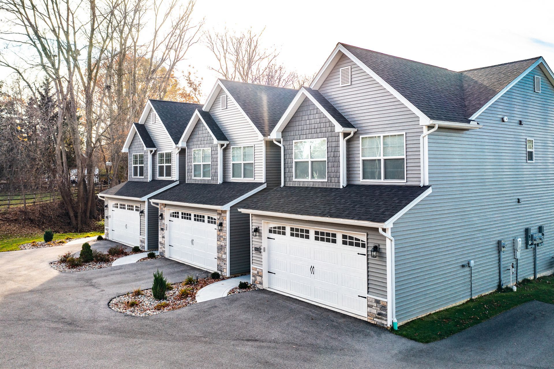 Row of attached suburban townhouses with gray roofs and white garage doors, viewed from the driveway