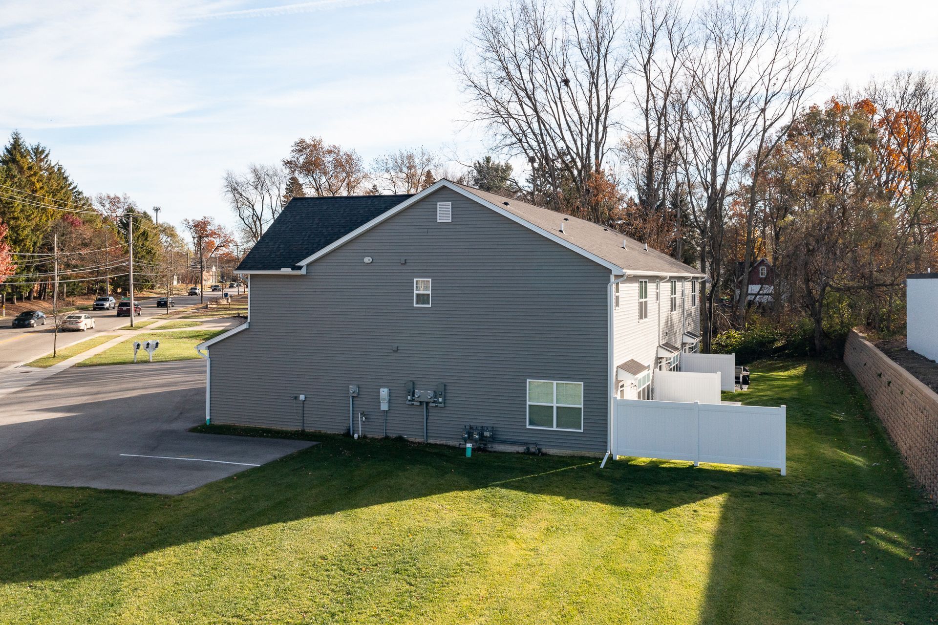 Side view of a gray house with a white fence and grassy yard under autumn trees