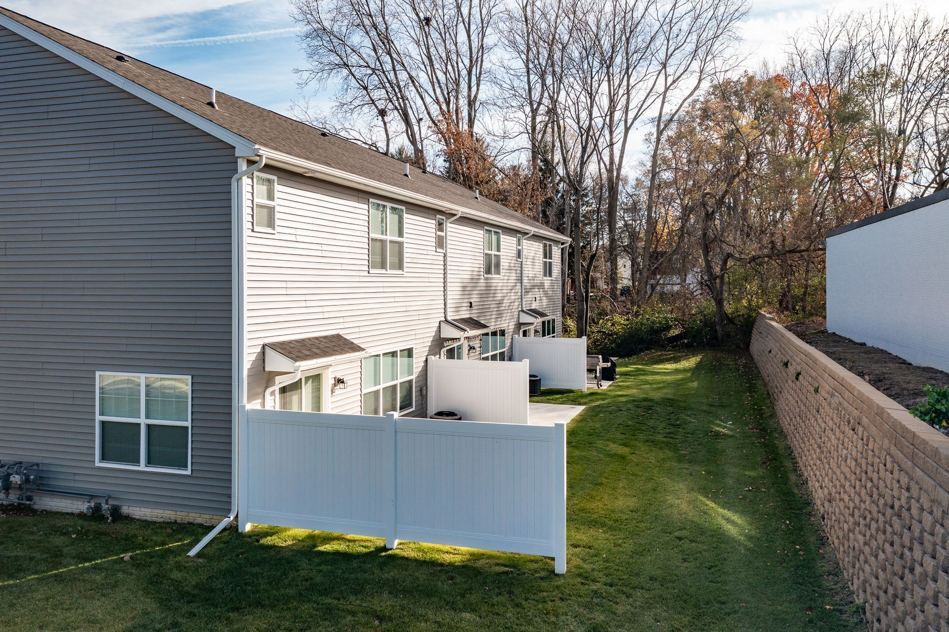 Suburban townhouse backyards with white fence, green lawn, and trees in fall.