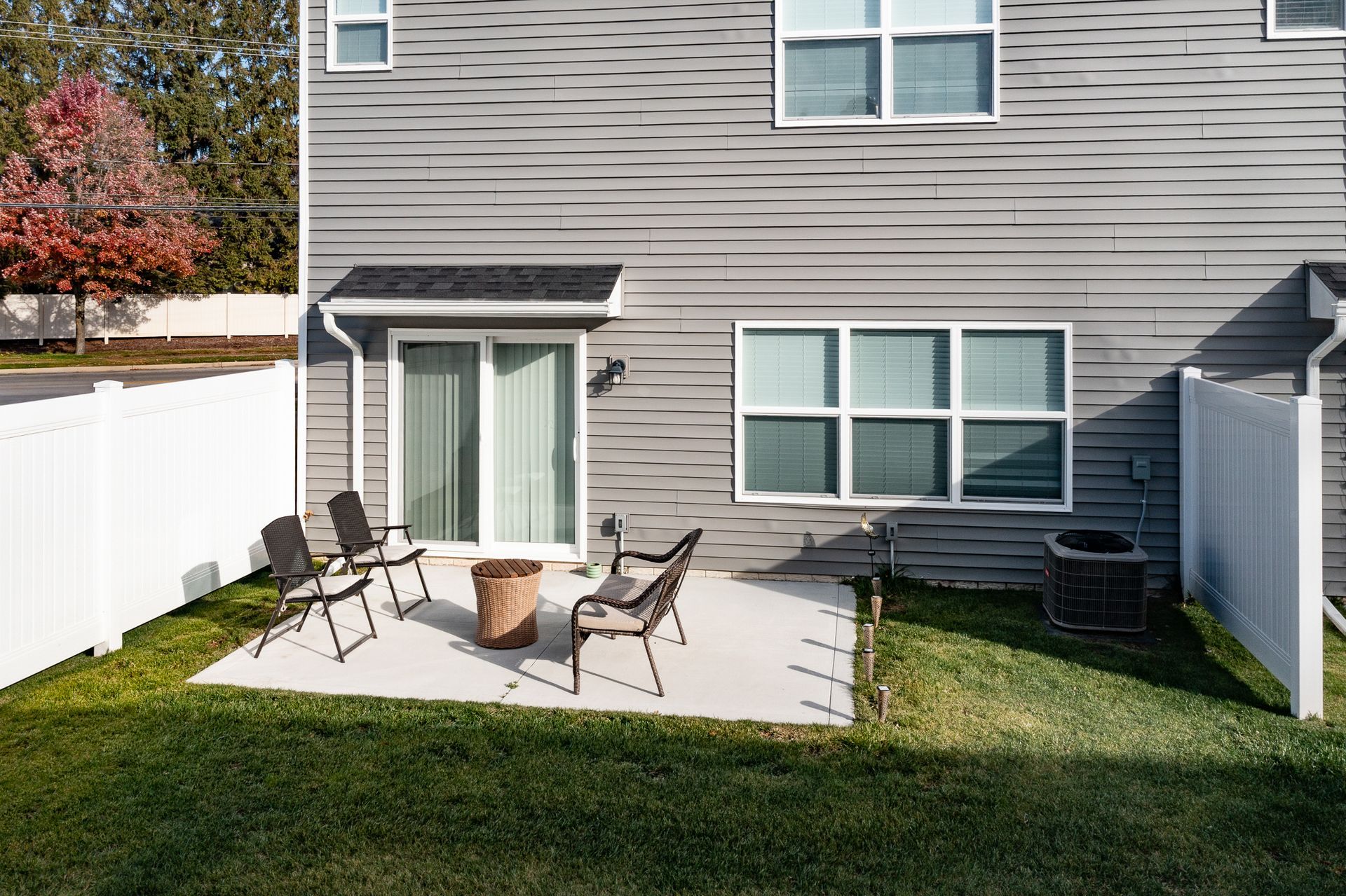 Backyard patio with chairs and fire pit beside a gray house and white fence