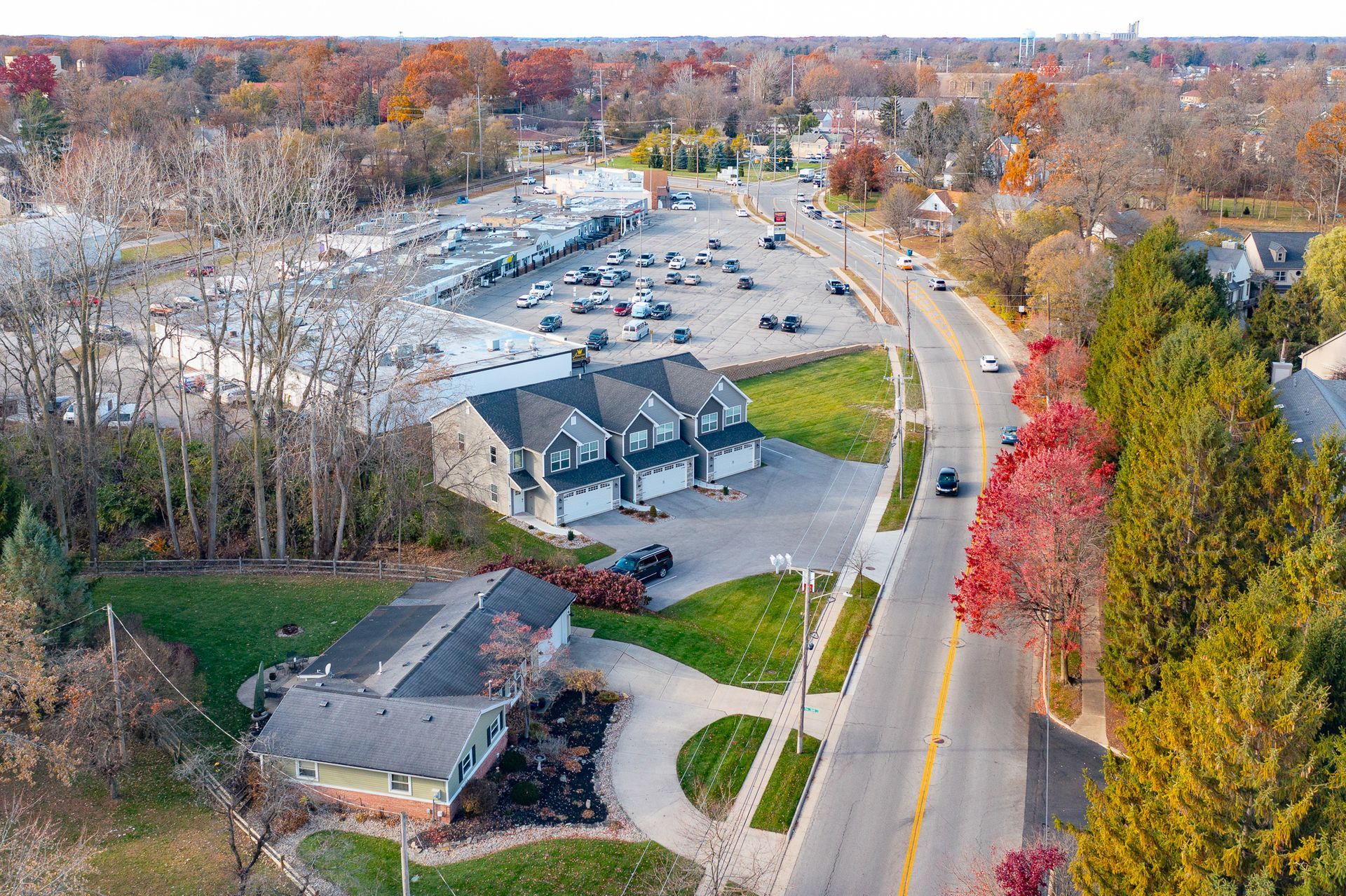 Aerial view of a suburban road lined with colorful autumn trees and houses
