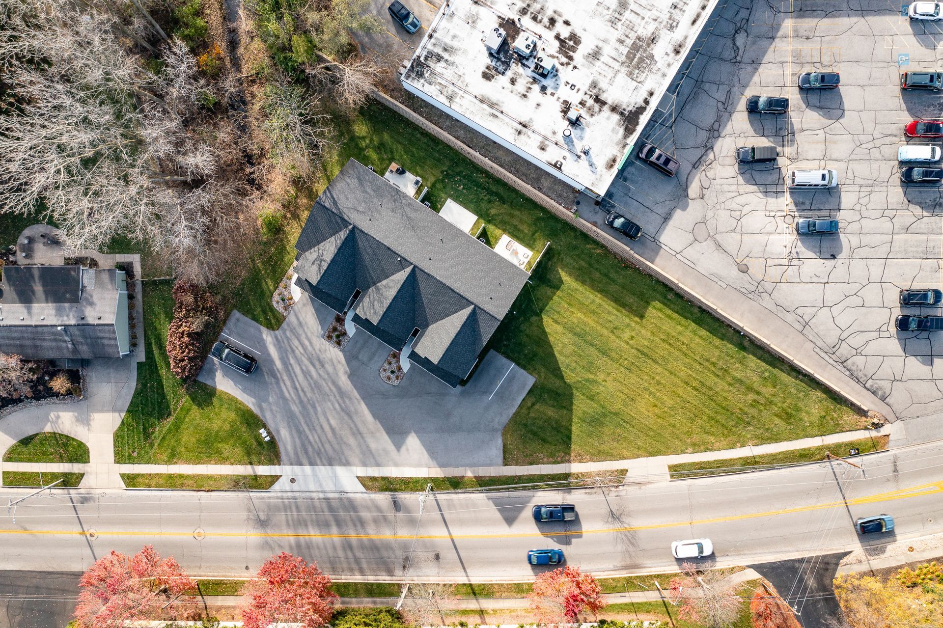 Aerial view of a house beside a road, parking lot, and grassy yard with a sidewalk.
