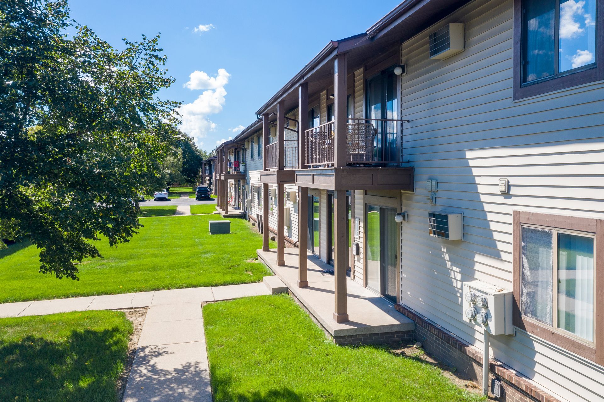 Apartment building with beige siding, wooden balconies, and a grassy courtyard under a bright blue sky