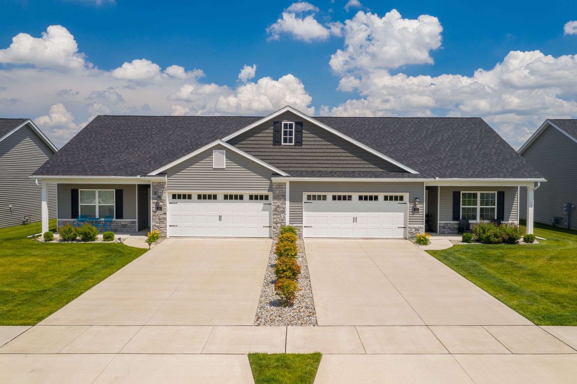 Modern duplex-style house with two garages, gray siding, and a wide concrete driveway under a blue sky