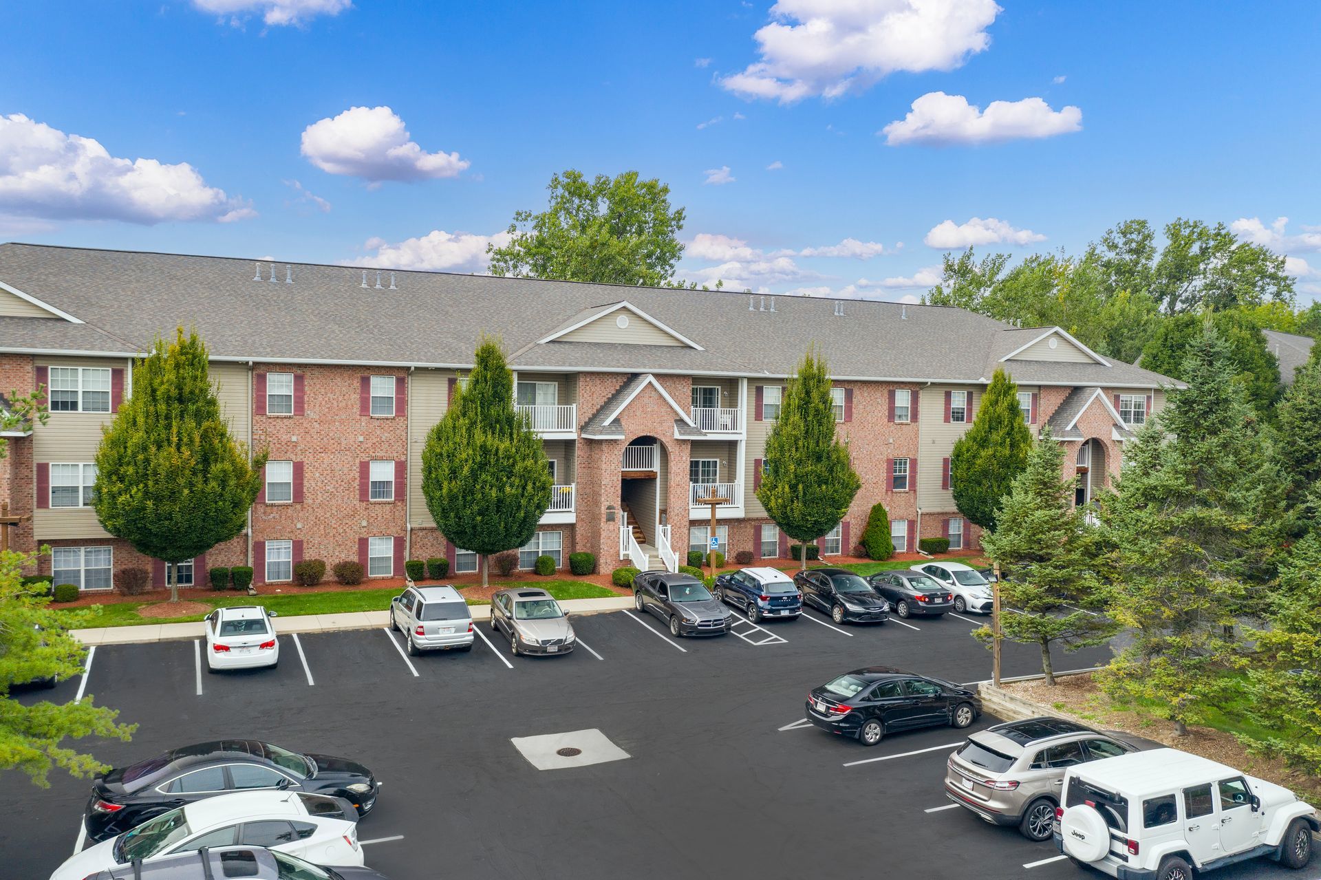 Brick apartment building with parked cars in a lot under a blue sky