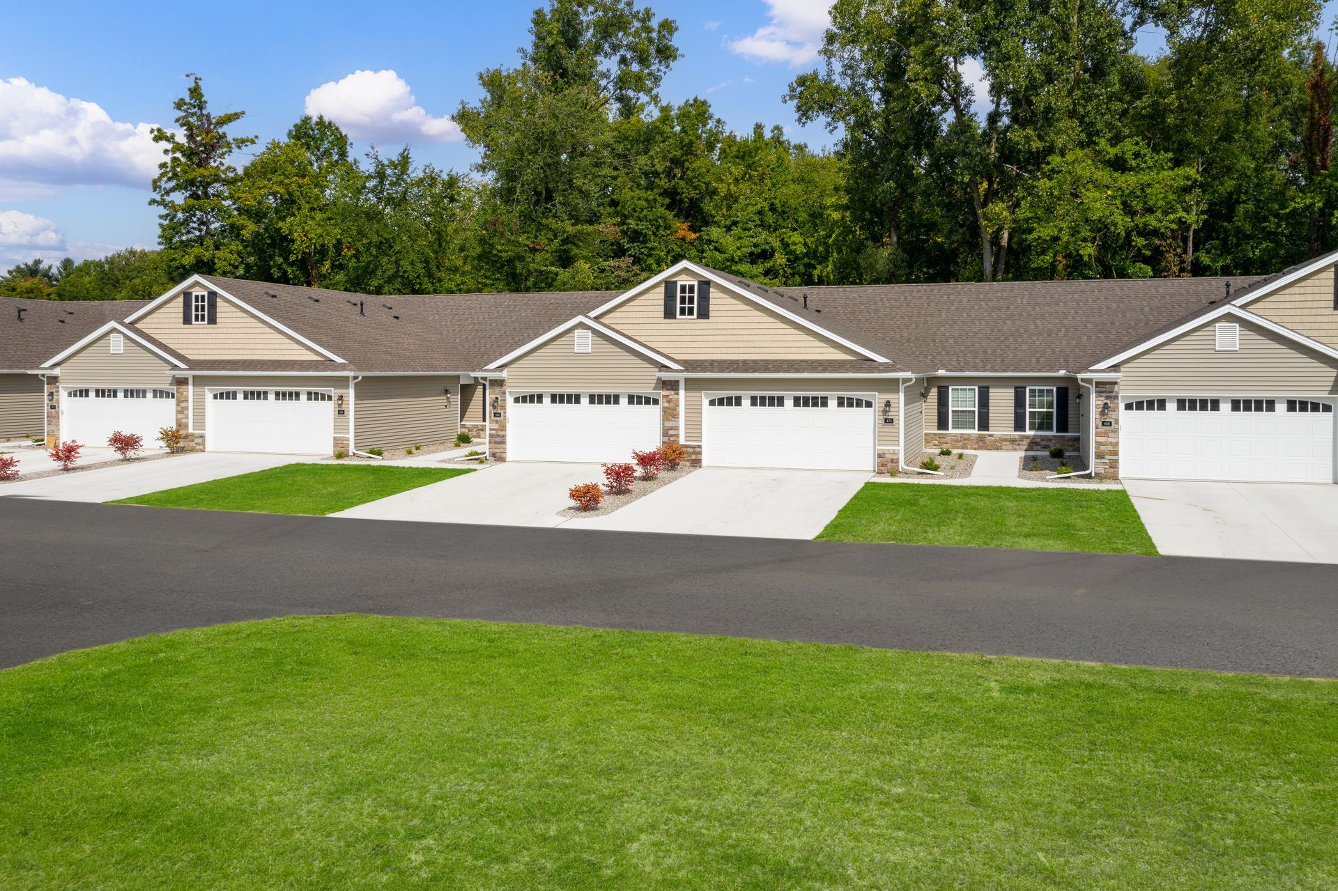 Row of beige townhomes with white garage doors and green lawns on a sunny day