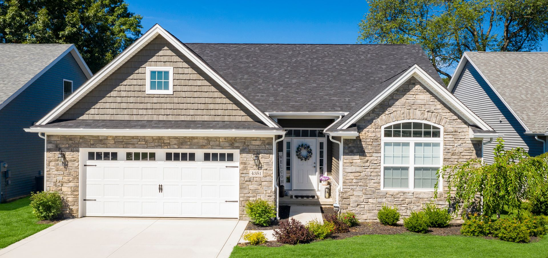 Suburban house with stone facade, white garage door, and front porch on a sunny day