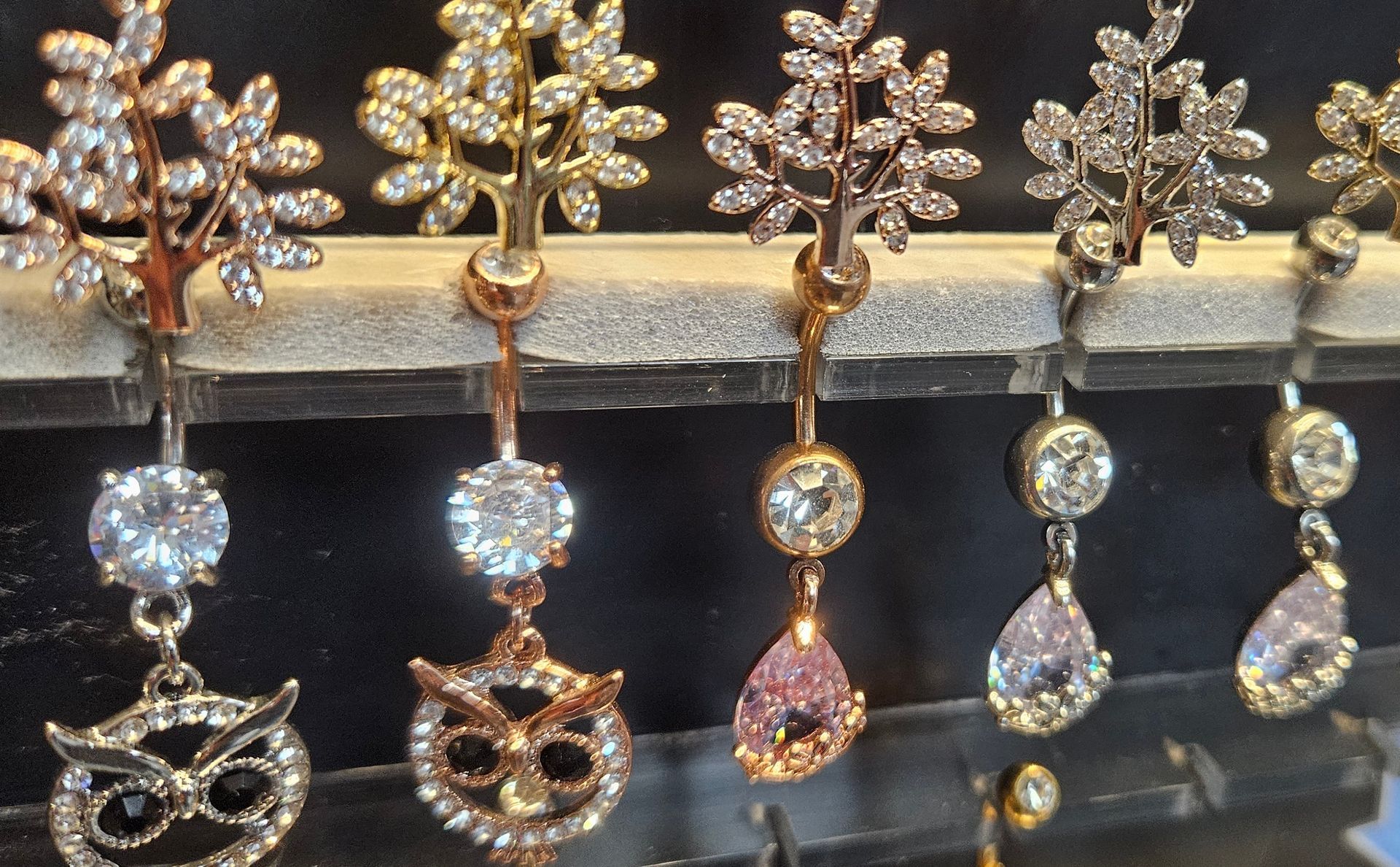 A close up look at a variety belly button jewelry covered in shinny gems and featuring a stylized owls head.