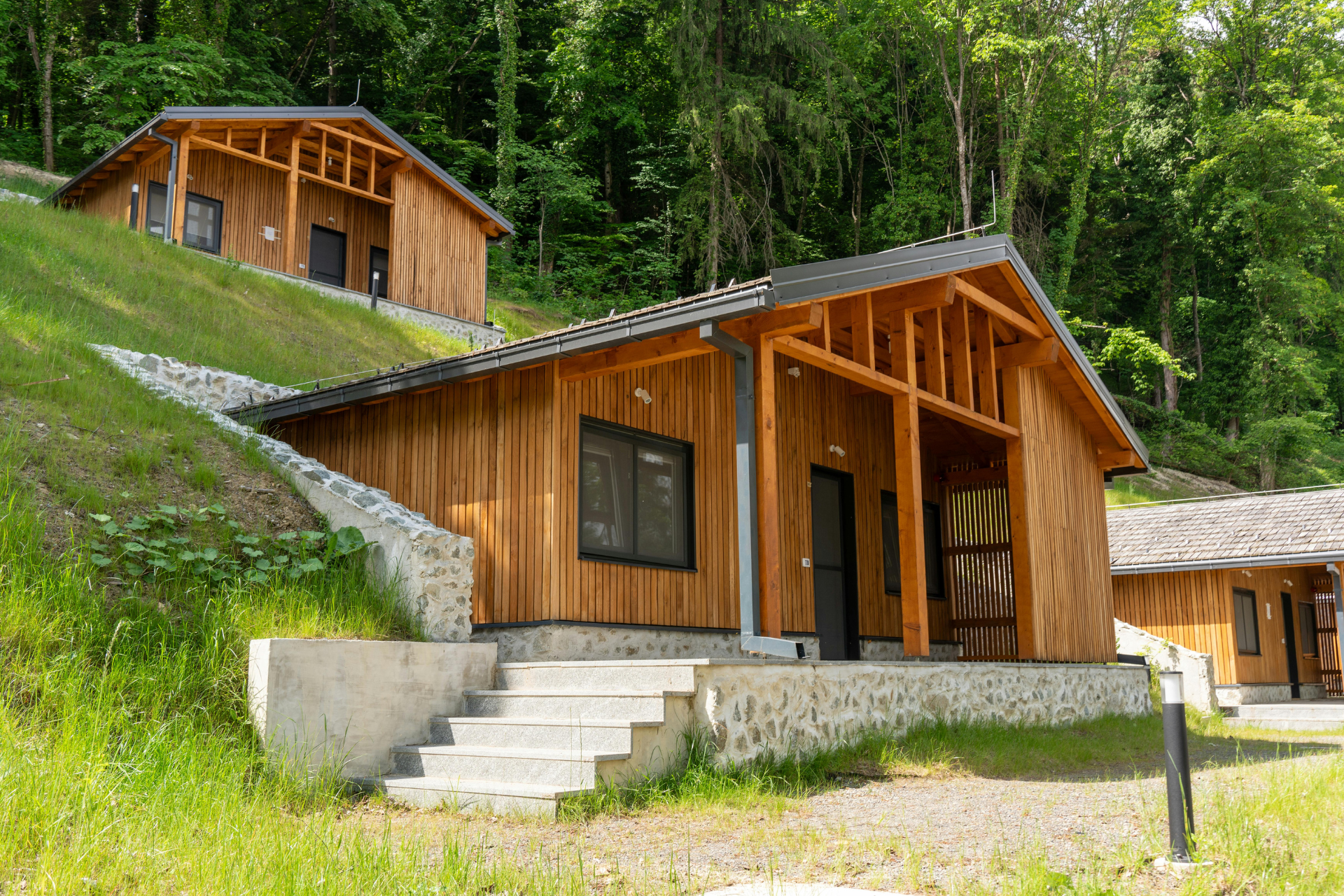 Wooden cabins on a hillside, with steps leading up to the entrance and surrounding greenery.