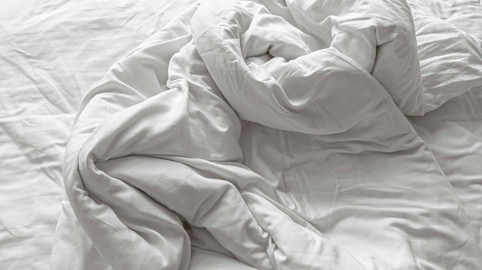 A bed with a white comforter and pillows on it.